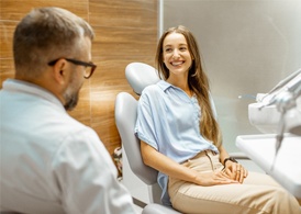 A young female sitting up in the dentist’s chair and smiling as she speaks to her dentist