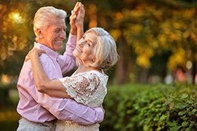 An older man and woman dancing together outside and enjoying life