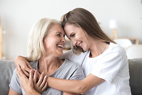 An older woman and her daughter sitting on a couch hugging and smiling