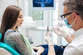 Dentist showing a dental implant to a young woman in the treatment chair