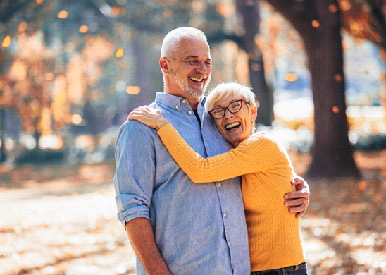 An older couple smiling and hugging outside after receiving dental implants near Palm Beach Gardens