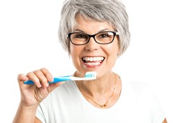 An older woman wearing glasses and holding a manual toothbrush in preparation for cleaning her teeth