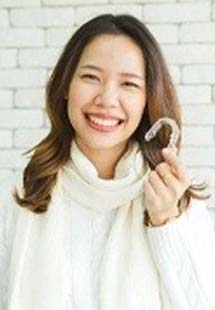 Smiling woman holding an Invisalign clear aligner