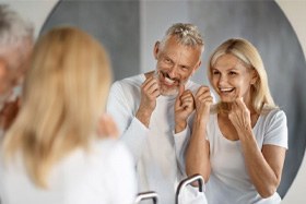 Older couple flossing their teeth in front of bathroom mirror