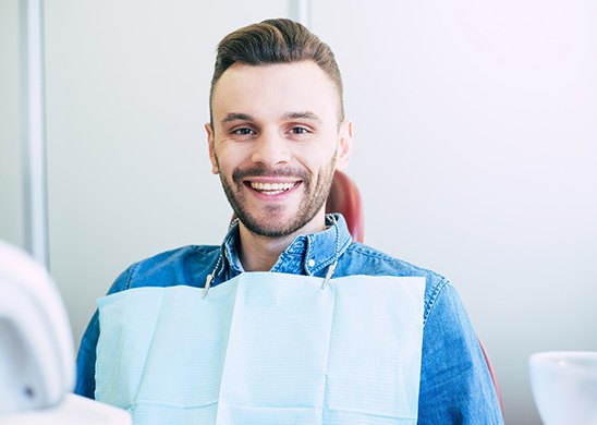 A young man with a beard smiling at his appointment in preparation for an oral cancer screening in Juno Beach