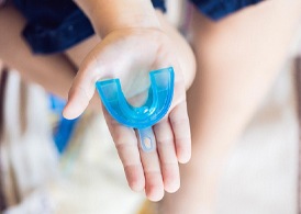 Hand holding mouthguard to prevent cracked teeth in Juno Beach