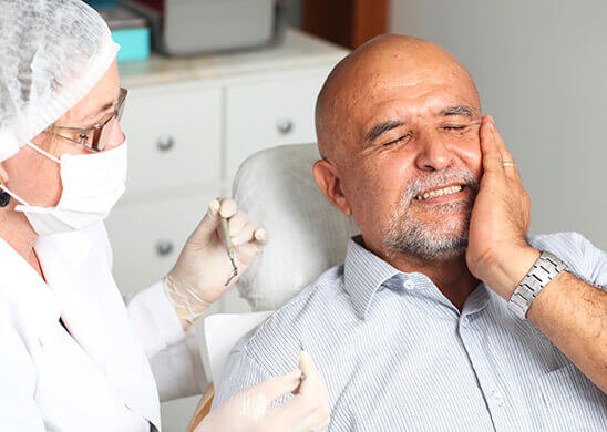 Older man in dental chair holding jaw
