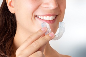 Smiling woman holding occlusal splint for TMJ treatment near Jupiter