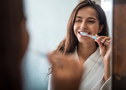 A young woman standing in front of her bathroom mirror brushing her teeth
