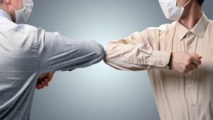 Two men in masks bumping elbows to greet each other