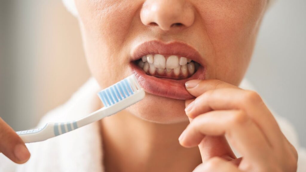A woman looking at her gums as she brushes her teeth