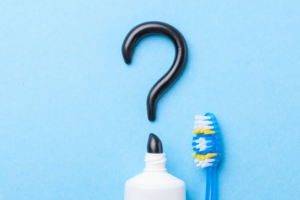 Charcoal toothpaste making a question mark on blue background next to toothbrush 