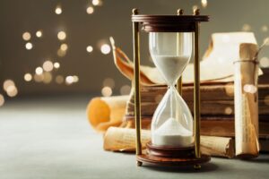 Hour-glass next to old rolls of parchment and sparkling lights in the background
